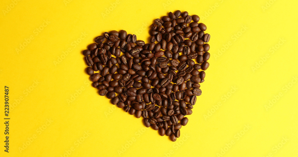 From above view of coffee beans laid in shape of heart on yellow background