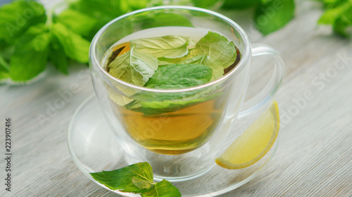 From above view of glass cup of green tea with leaves of mint and slice of lemon placed on saucer on wooden background