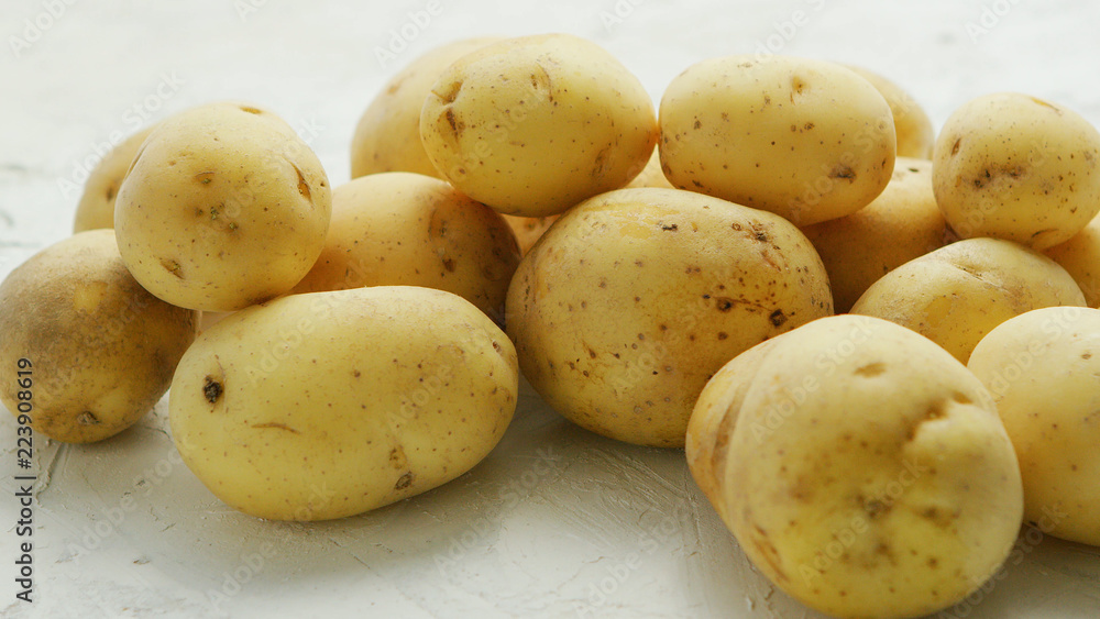 Closeup shot of pile of unpeeled clean potatoes composed on white surface in daylight Closeup shot of pile of unpeeled clean potatoes composed on white surface in daylight