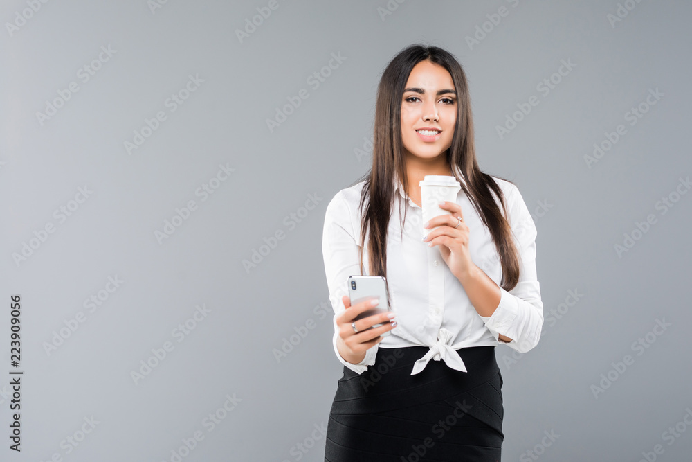 Portrait of satisfied young business woman using mobile phone while holding cup of coffee to go isolated over white background Portrait of satisfied young business woman using mobile phone while holding cup of coffee to go isolated over white background