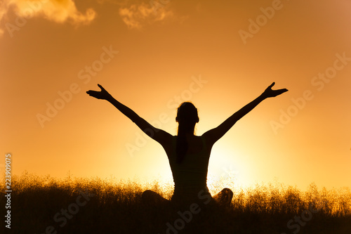 People feeling happy and personal wellbeing. Happy female sitting outdoors with arms up facing the sunset.
