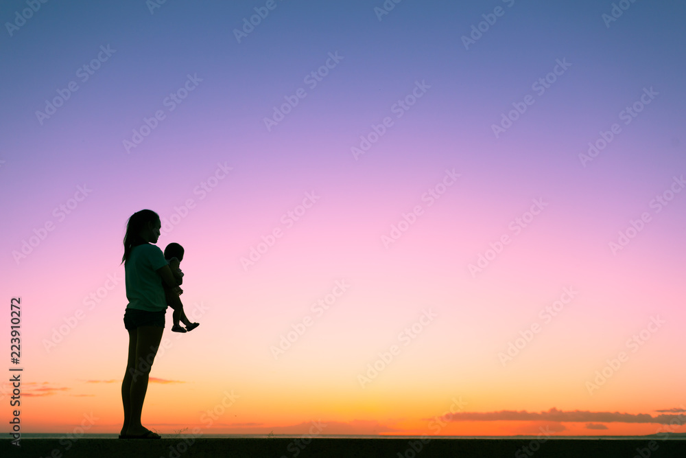 Silhouette of mother holding her little baby girl watching the sunset. Motherhood, parenting concepts.