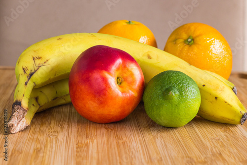 A healthy fruit arrangement with a red nectarine, a green lime, two bananas and two oranges, lying on a bamboo plate. sweet fruits as a healty snack with lots of vitamins