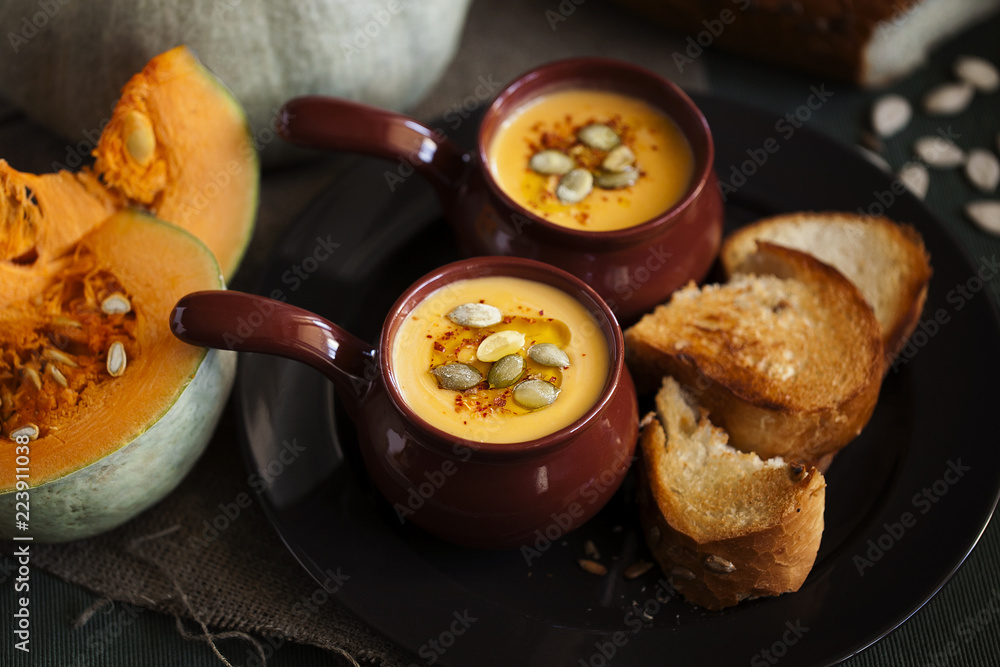 Autumn homemade cream soup of roasted pumpkin with croutons or toasted bread and seeds in a vintage ceramic bowls for Halloween or Thanksgiving day close-up on dark background.Healthy vegan food Autumn homemade cream soup of roasted pumpkin with croutons or toasted bread and seeds in a vintage ceramic bowls for Halloween or Thanksgiving day close-up on dark background.Healthy vegan food