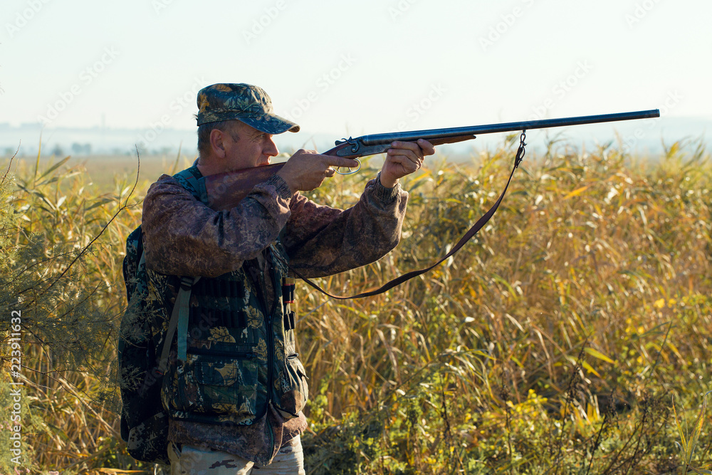 Fototapeta premium Silhouette of a hunter with a gun in the reeds against the sun, an ambush for ducks with dogs