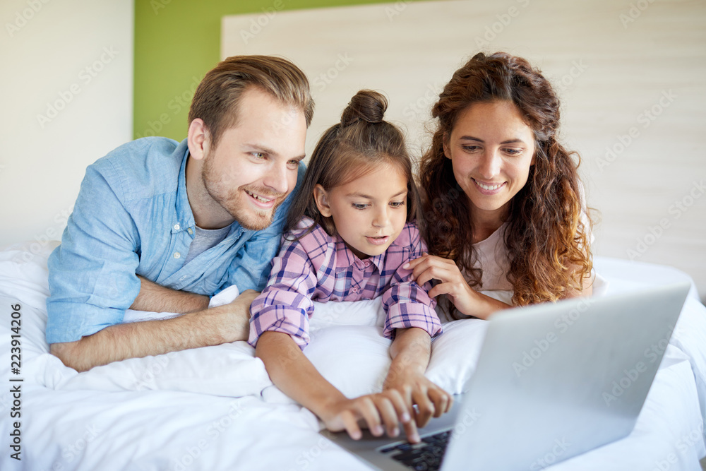 Happy young couple with their little daughter choosing video or mobie to watch on weekend Happy young couple with their little daughter choosing video or mobie to watch on weekend