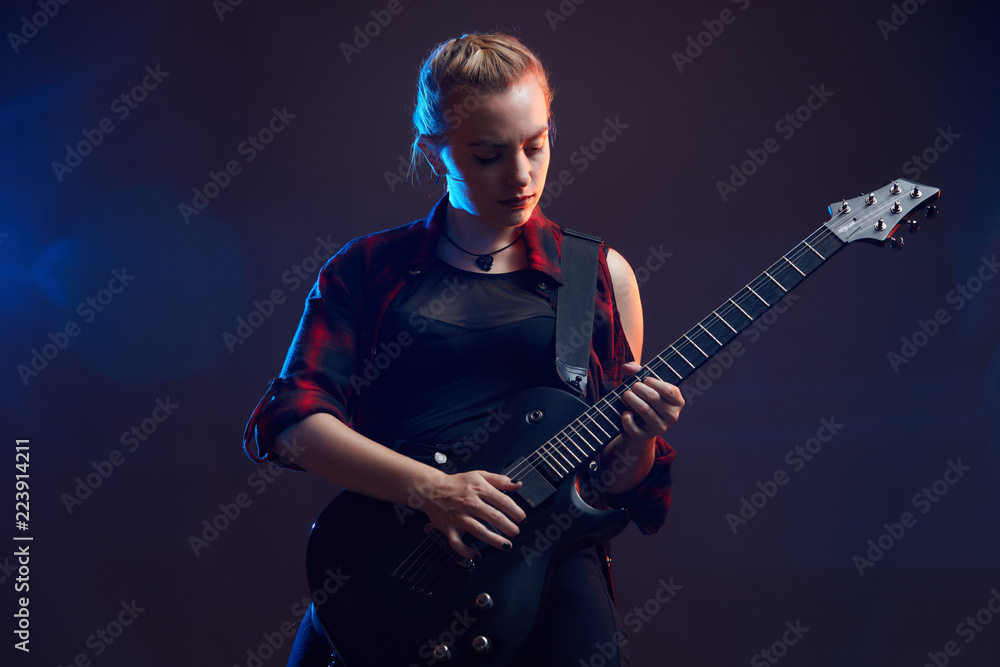 Fototapeta premium Blonde woman play guitar on stage, red, blue light dark scene