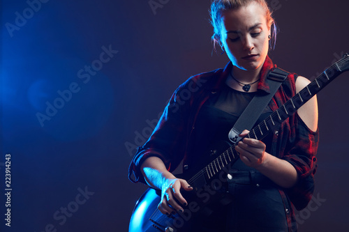 Blonde woman play guitar on stage, red, blue light dark scene