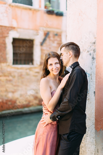Romantic couple in Venice. Young woman and man in elegant clothes hugging near the venetian canal and ancient buildings. Italy, Europe.