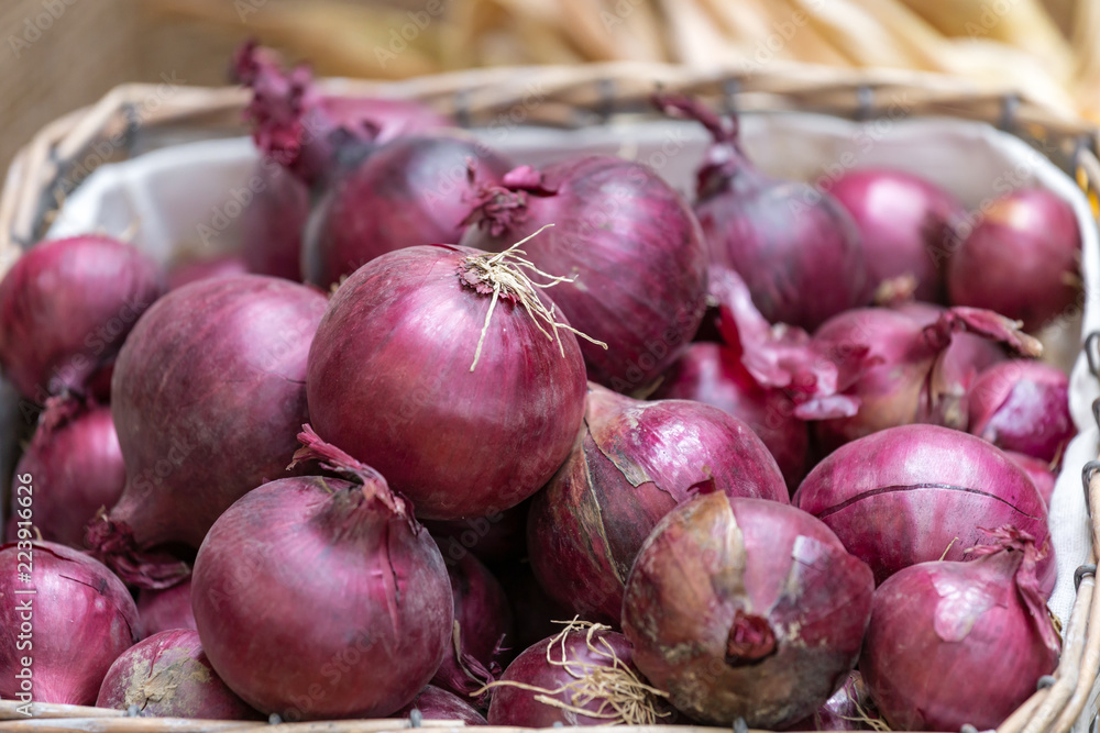 Marktstand mit roten Zwiebeln im Korb auf Stroh