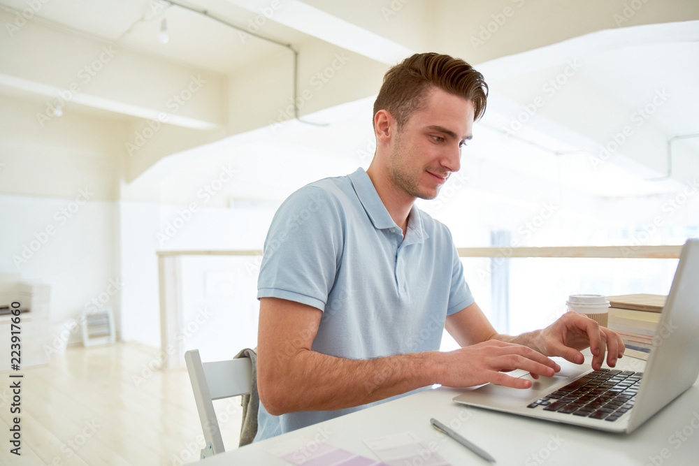 Young designer sitting in front of laptop and looking for websites with information about new trends Young designer sitting in front of laptop and looking for websites with information about new trends