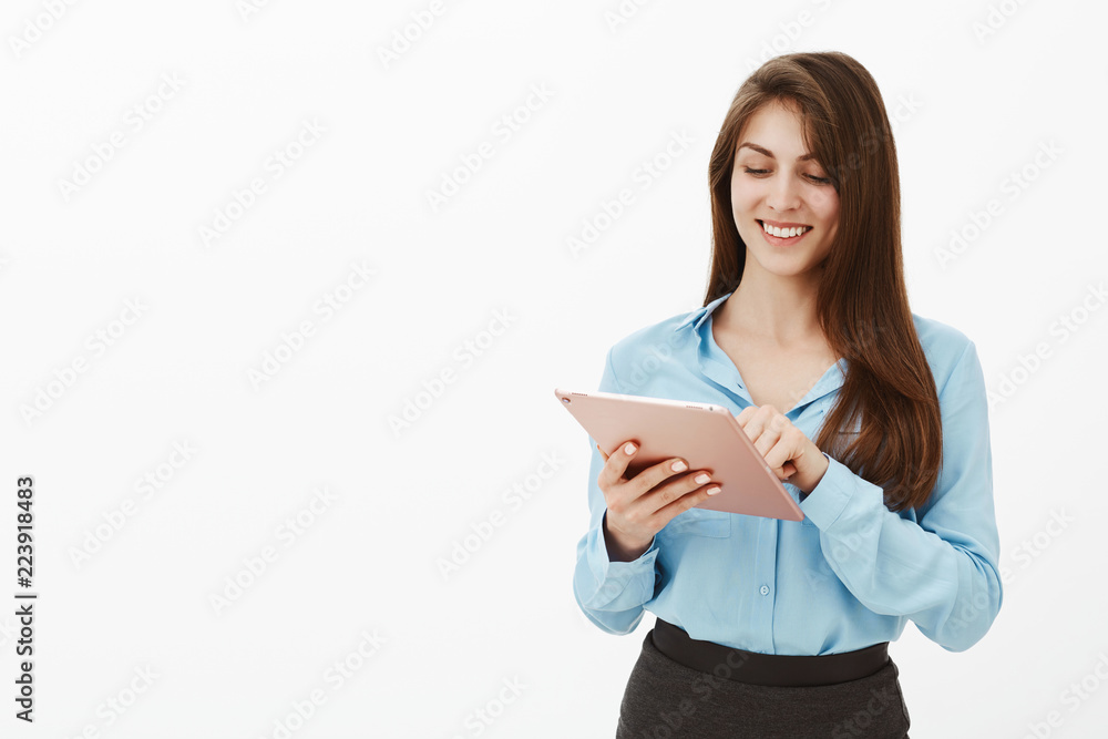 Office manager helping customer create account. Positive charming female entrepreneur in blue blouse, typing message in pink digital tablet and smiling broadly, being carefree and satisfied Office manager helping customer create account. Positive charming female entrepreneur in blue blouse, typing message in pink digital tablet and smiling broadly, being carefree and satisfied