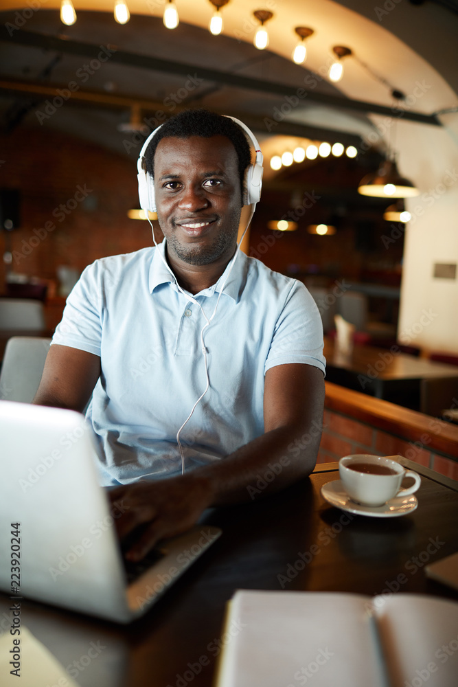 Happy young businessman with headphones sitting in cafe in front of laptop and networking Happy young businessman with headphones sitting in cafe in front of laptop and networking