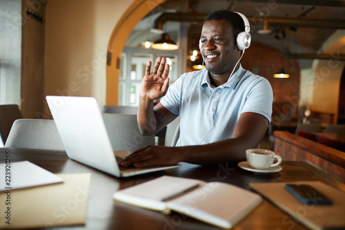 African-american businessman waving his hand to someone on laptop display while communicating through video-chat