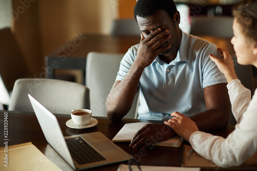 Young businessman in trouble sharing his problem with female colleague who comforting him