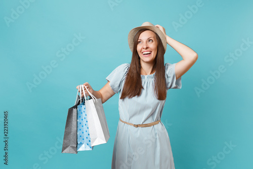 Portrait fashionable smiling beautiful caucasian woman in summer dress, straw hat holding packages bags with purchases after shopping isolated on blue pastel background. Copy space for advertisement.