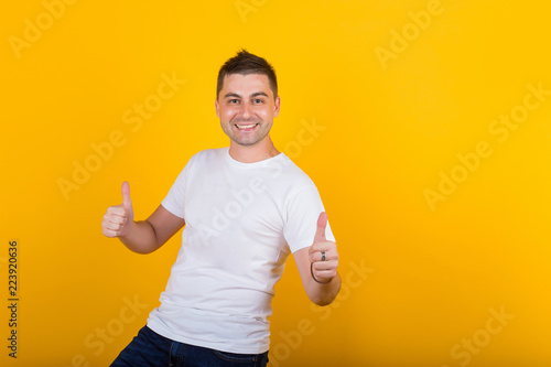 Handsome, cheerful, positive guy in jeans and a white T-shirt on a yellow background