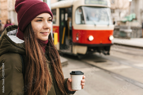 Canvas Print A girl drinks coffee from a disposable cup on the street in Prague near the tram stop