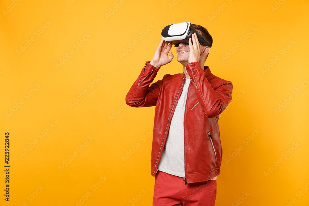 Portrait vogue fun young man in red leather jacket t-shirt looking up in headset standing isolated on bright trending yellow background. People sincere emotions lifestyle concept. Advertising area. Portrait vogue fun young man in red leather jacket t-shirt looking up in headset standing isolated on bright trending yellow background. People sincere emotions lifestyle concept. Advertising area.