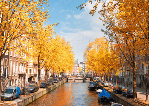 One of canals in Amsterdam old town with green trees at fall day, Holland