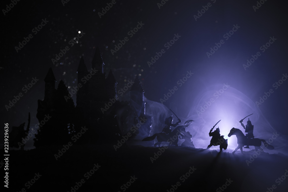 Medieval battle scene with cavalry and infantry. Silhouettes of figures as separate objects, fight between warriors on dark toned foggy background with medieval castle. Night scene. Selective focus
