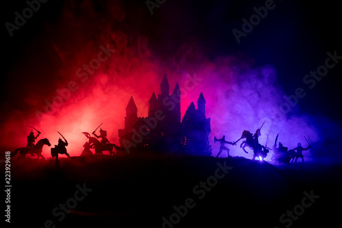 Medieval battle scene with cavalry and infantry. Silhouettes of figures as separate objects, fight between warriors on dark toned foggy background with medieval castle. Night scene. Selective focus