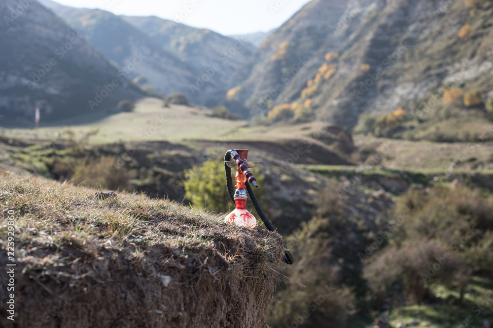 Hookah, traditional arabic waterpipe, direct sunset light, outdoor photo. Mountain background or Silhouettes of hookah on sunset background. Outdoor. Selective focus