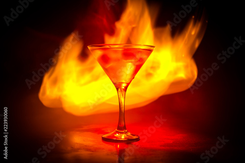 Martini in fire concept. Glass of famous cocktail Martini burning in fire at dark toned foggy background.
