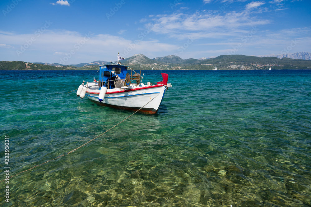White fisher boat floats on crystal clear water in Greece