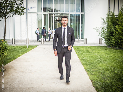 Portrait of stylish young man wearing business suit, standing in modern city setting © theartofphoto
