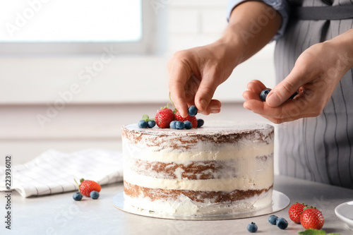 Woman decorating delicious cake with fresh berries at table. Homemade pastry