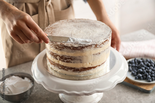 Woman decorating delicious cake with fresh cream on stand. Homemade pastry photo