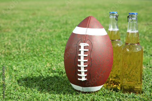 Ball for American football and beverage on fresh green field grass. Space for text