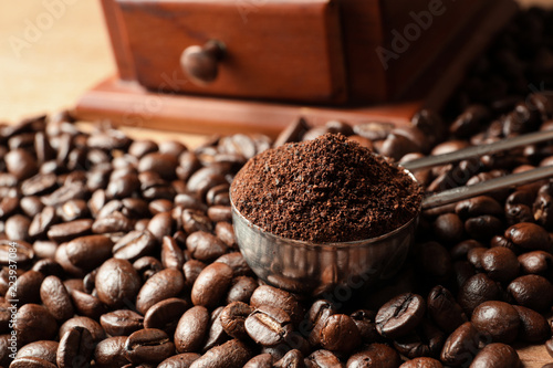 Spoon with coffee grounds and roasted beans on table, closeup