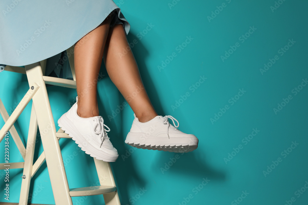 Woman in stylish sneakers on ladder near color wall, closeup. Space for text - obrazy, fototapety, plakaty 