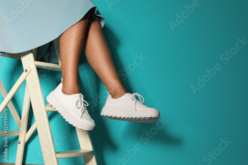 Woman in stylish sneakers on ladder near color wall, closeup. Space for text