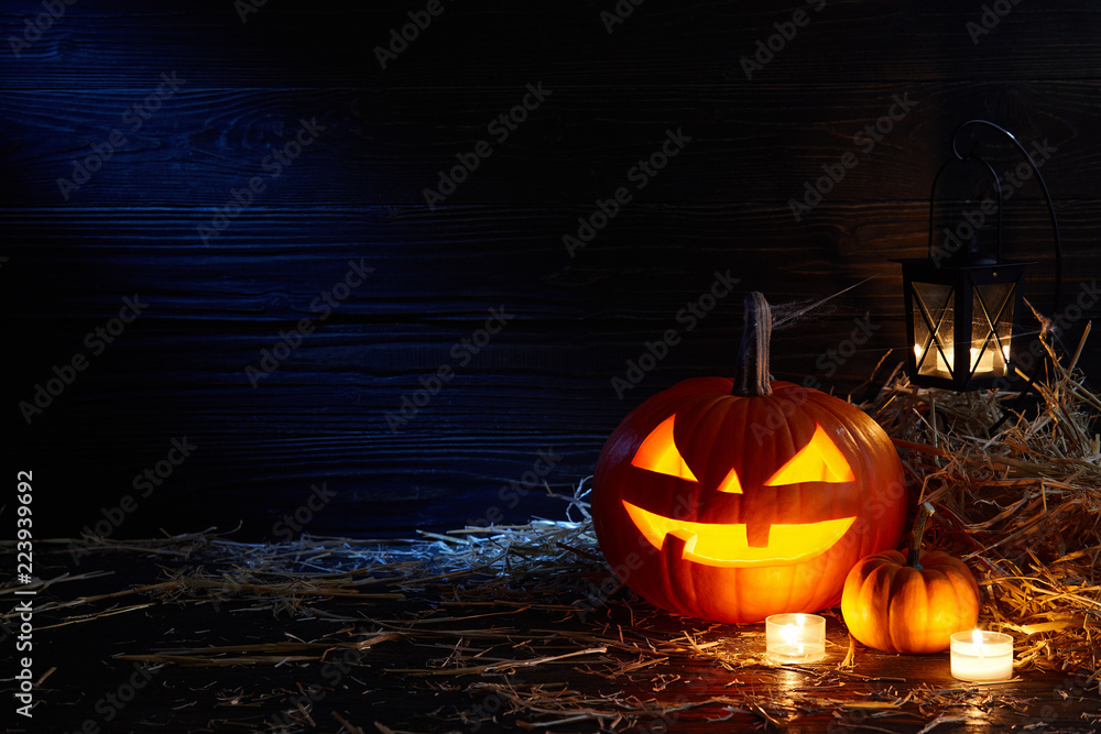 Fototapeta premium Carved pumpkin or jack-o-lantern in dark barn, Halloween holiday celebration concept