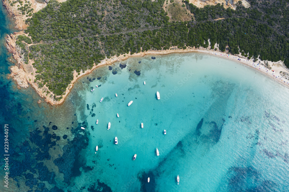 Spectacular aerial view of some yachts and small boats floating on a clear and turquoise sea, Sardinia, Italy.