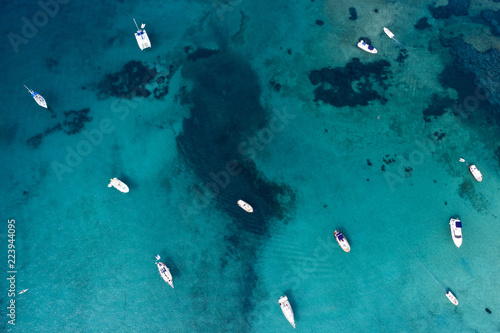 Spectacular aerial view of some yachts and small boats floating on a clear and turquoise sea, Sardinia, Italy.