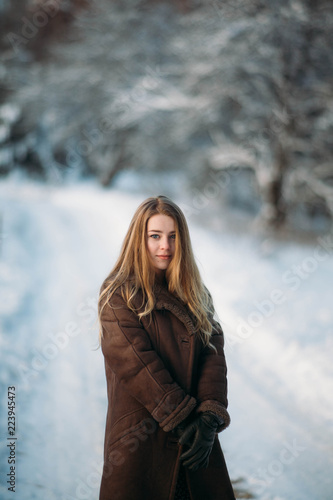 girl blonde in winter dress in snowy forest walking. frosty sunny morning in nature.