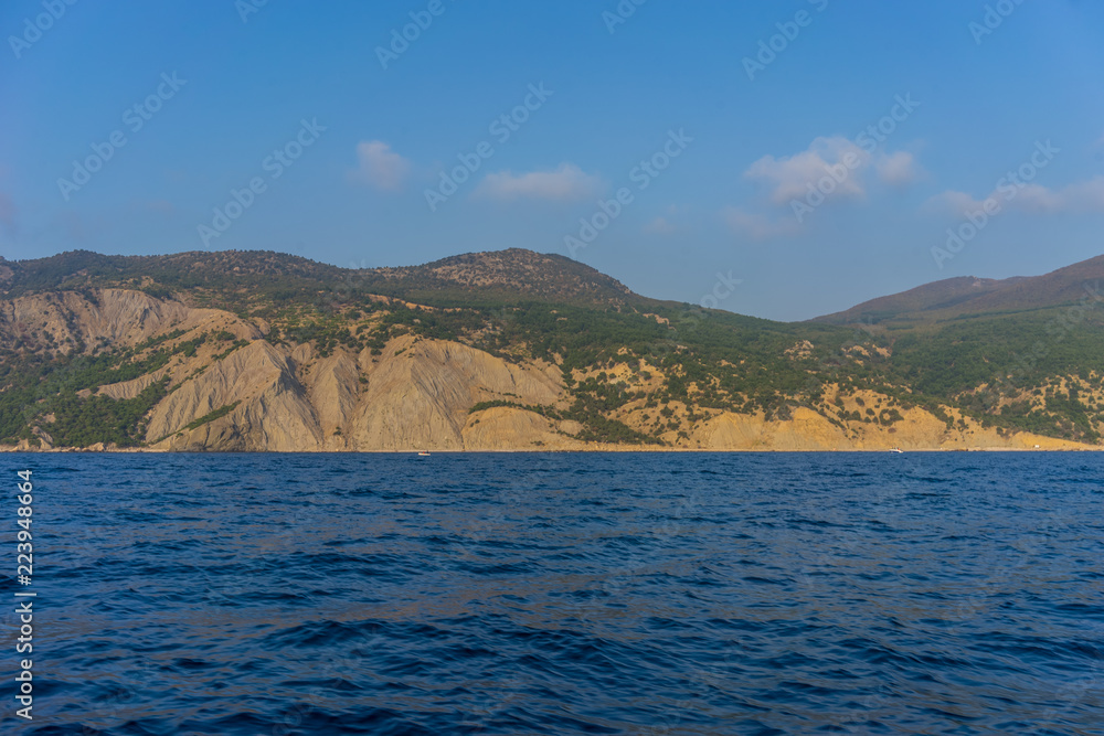 Shoreline with hills covered with vegetation against the blue of sea and sky with clouds Shoreline with hills covered with vegetation against the blue of sea and sky with clouds