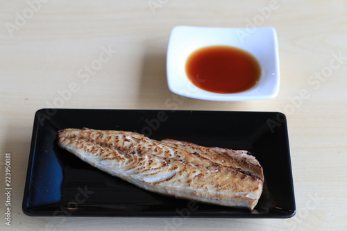 Grilled saba on black dish with dipping soy sauce and green spicy sauce on wooden table
