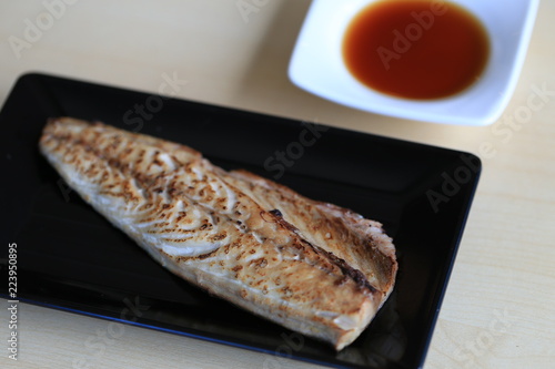 Grilled saba on black dish with dipping soy sauce and green spicy sauce on wooden table
