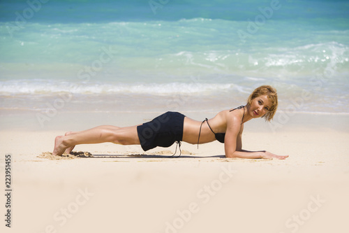 isolated portrait of young happy and beautiful sporty and fit woman doing plank exercise on beach sand smiling cheerful in wellness fitness and healthy lifestyle concept
