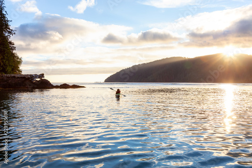 Girl kayaking in the Pacific Ocean during a cloudy summer sunset. Taken in San Josef Bay, Cape Scott, Northern Vancouver Island, BC, Canada.