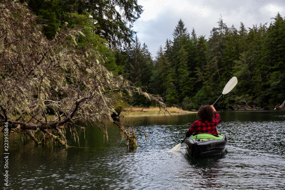 Girl kayaking in a river during a cloudy summer day. Taken in Cape Scott Provincial Park, Northern Vancouver Island, BC, Canada.