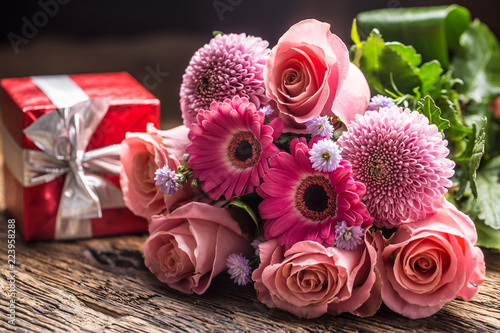 Beautiful bouquet of flowers with red gift on wooden table.
