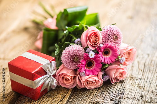 Beautiful bouquet of flowers with red gift on wooden table.