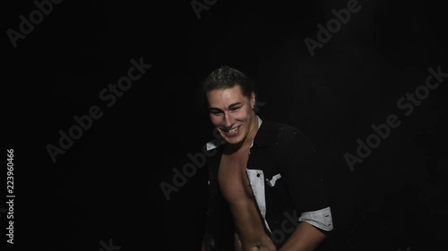 Someone is throwing white powder on handsome athletic young brown eyed male dressed in unbuttoned shirt with tattoo on chest in front of camera on black matte background. photo