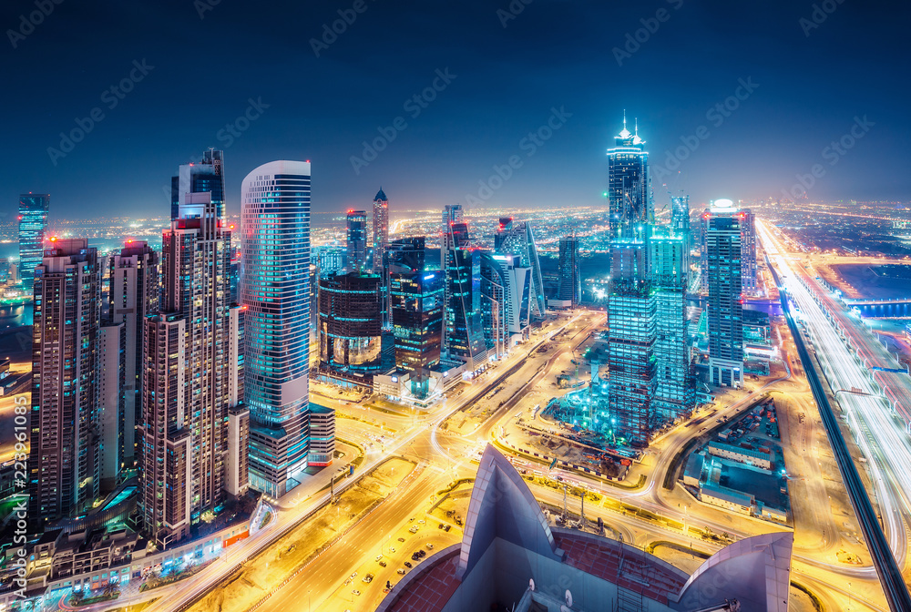 Naklejka premium Spektakularna miejska panorama z kolorowymi iluminacjami miasta. Widok z lotu ptaka na autostrady i drapacze chmur w Dubaju, w Zjednoczonych Emiratach Arabskich.